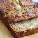 Slice of homemade rhubarb banana bread on a wooden table.