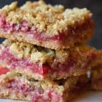 Freshly baked strawberry rhubarb crumb bars on a white plate